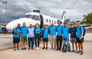 Team in blue shirts posing with a small airplane on tarmac
